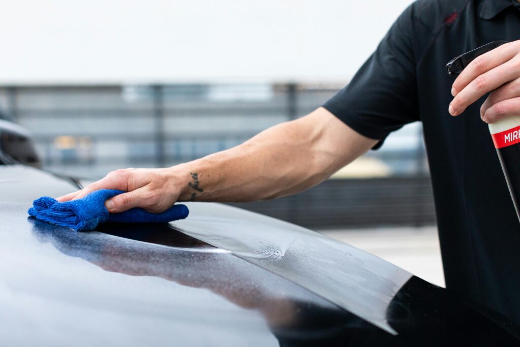 pexels-photo-7154630-7154630 Close-up of hand cleaning car with cloth and spray bottle for maintenance.